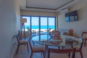 A modern dining area with a glass table, wooden chairs, and a view of the beach. - Ocean Heaven: New Downtown Condo (Isla Mujeres)