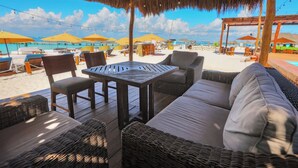 An outdoor seating area with wicker furniture, a table, and umbrellas. - Ocean Heaven: New Downtown Condo (Isla Mujeres)