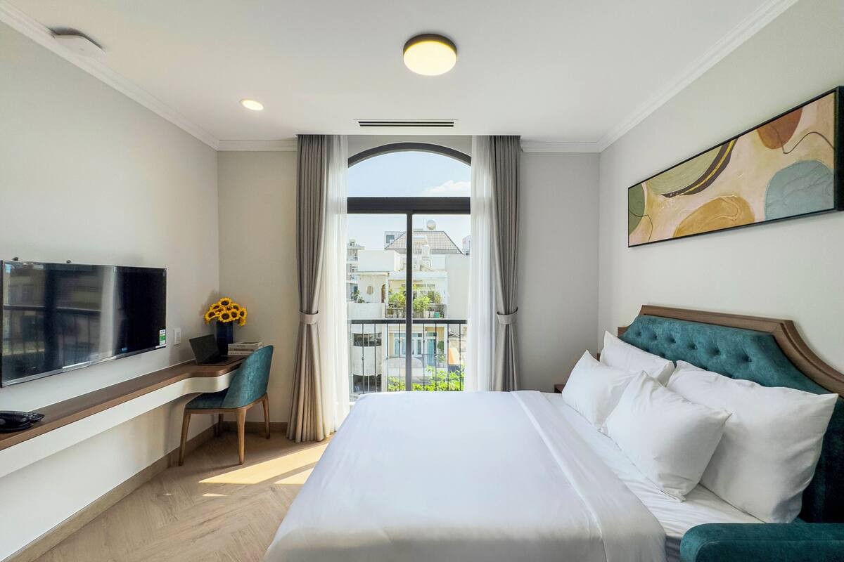 Ein Hotelzimmer mit Bett, Schreibtisch, Stuhl, Fernseher und einem großen Fenster mit Vorhängen.