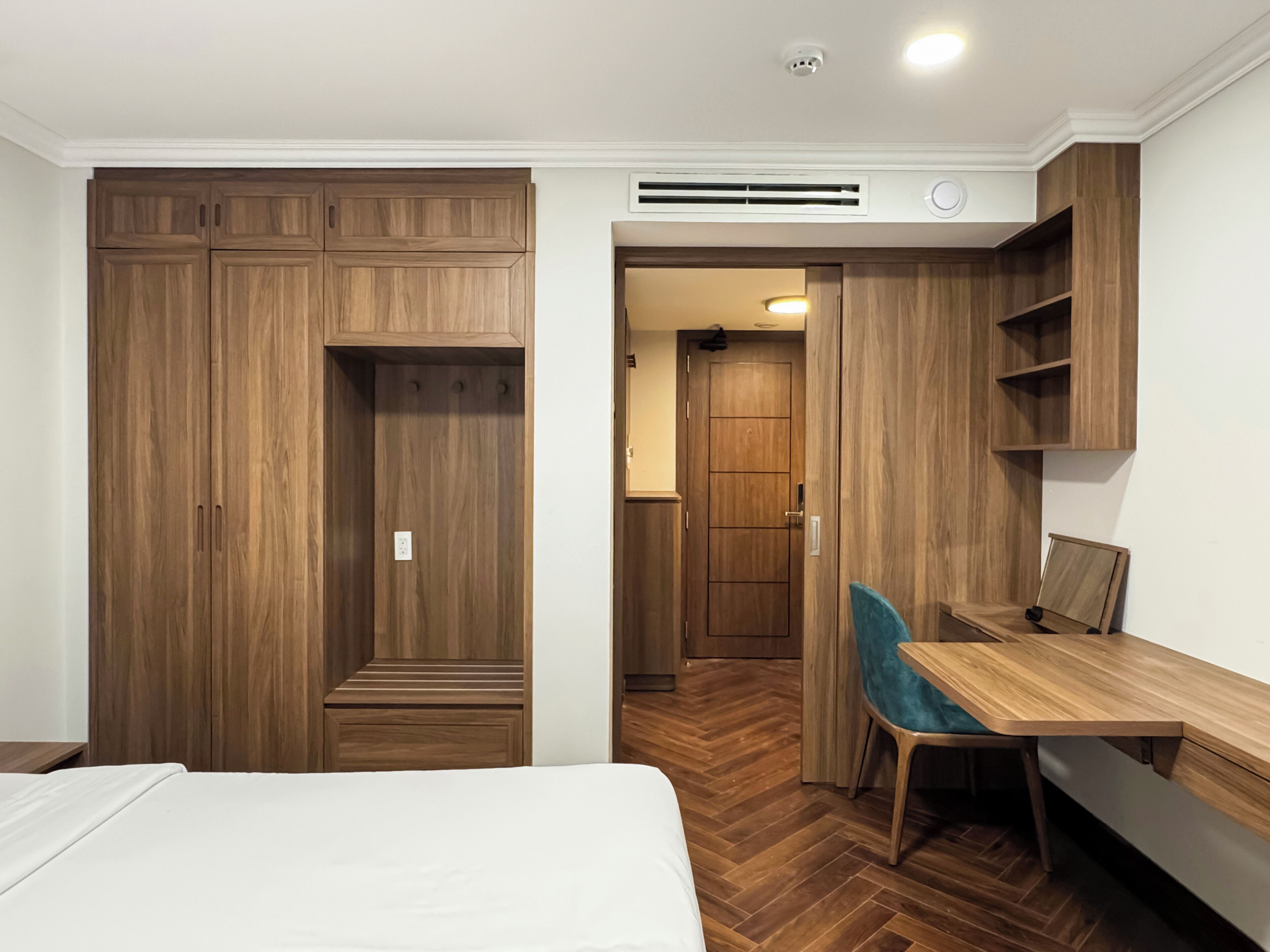 Een slaapkamer met een grote kledingkast, een bureau met stoel en een vloer van hout met een chevronsmotief.