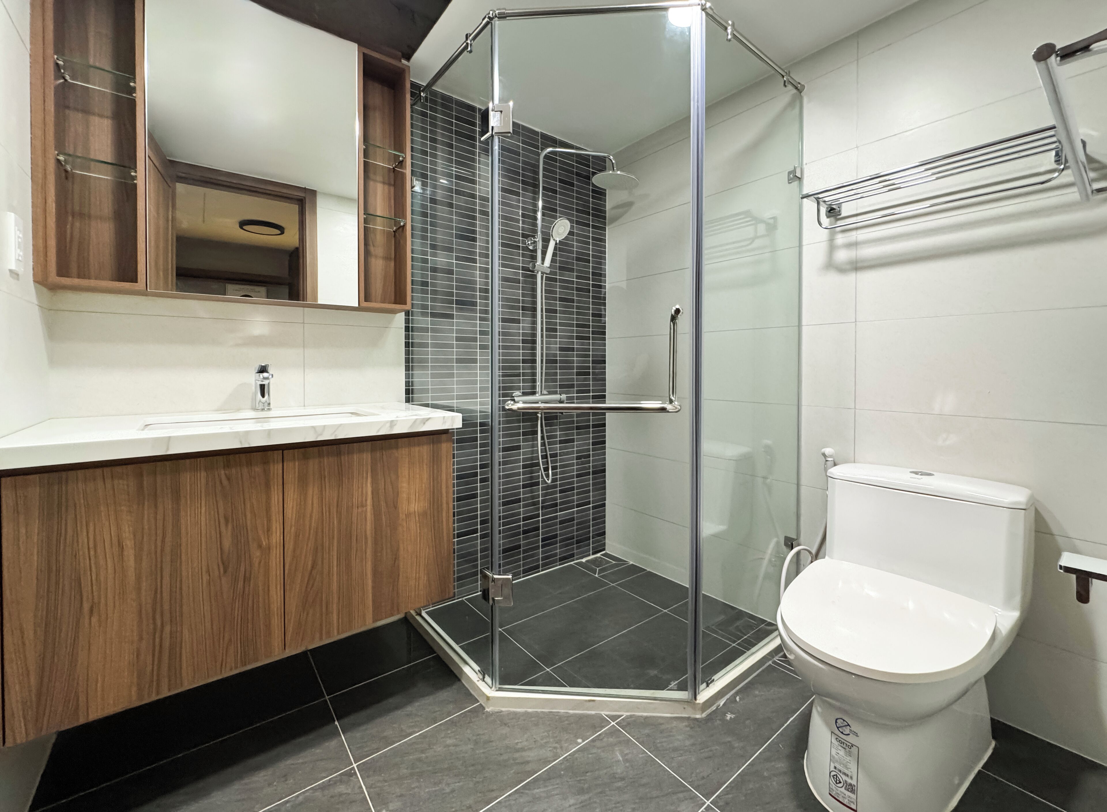 Une salle de bain moderne avec une douche à parois de verre, des toilettes blanches et un meuble-lavabo en bois avec un miroir.