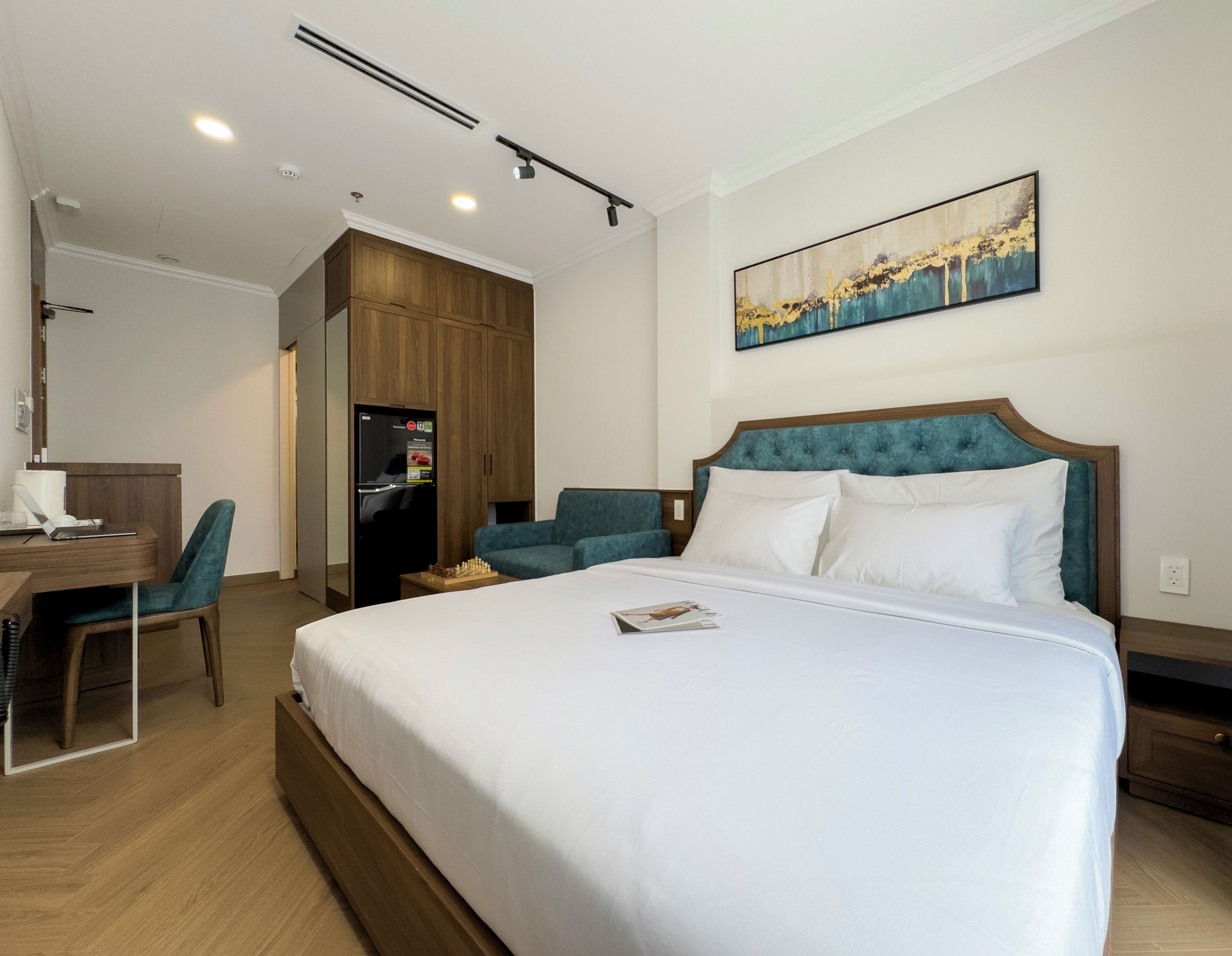 Una camera d'albergo con un letto grande, una scrivania con un portatile, una sedia, un armadio e un quadro appeso al muro.