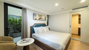 Une chambre d’hôtel moderne avec un grand lit, une petite table ronde, un canapé et une porte-fenêtre coulissante donnant sur un balcon agrémenté de plantes.