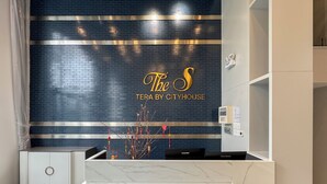 Un comptoir d’accueil avec un mur recouvert de carreaux bleu foncé, une branche décorative ornée de divers objets, et une enseigne indiquant : « The S TERA BY CITYHOUSE ».