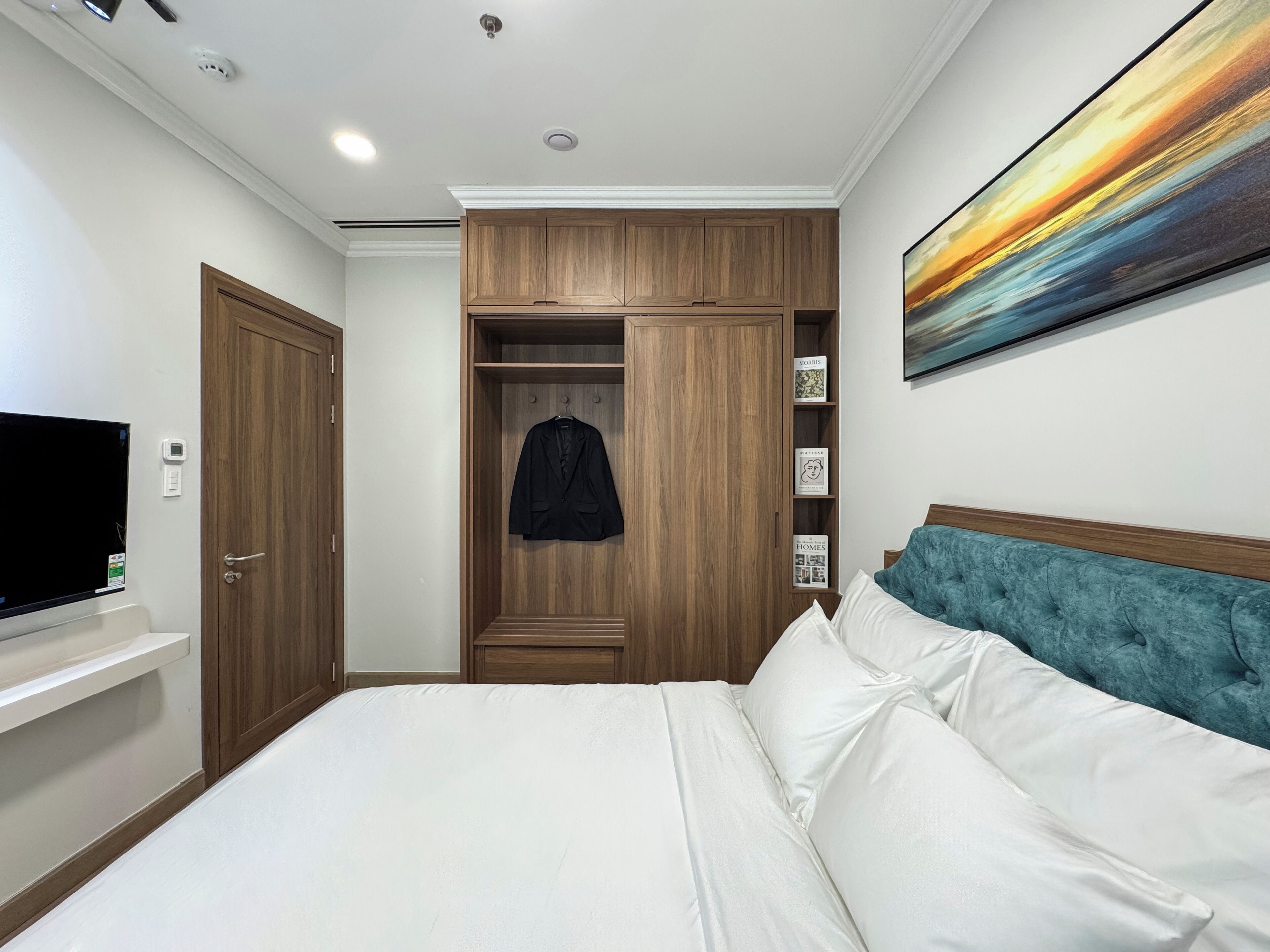 Une chambre à coucher avec un lit, une armoire, un téléviseur et un tableau accroché au mur.