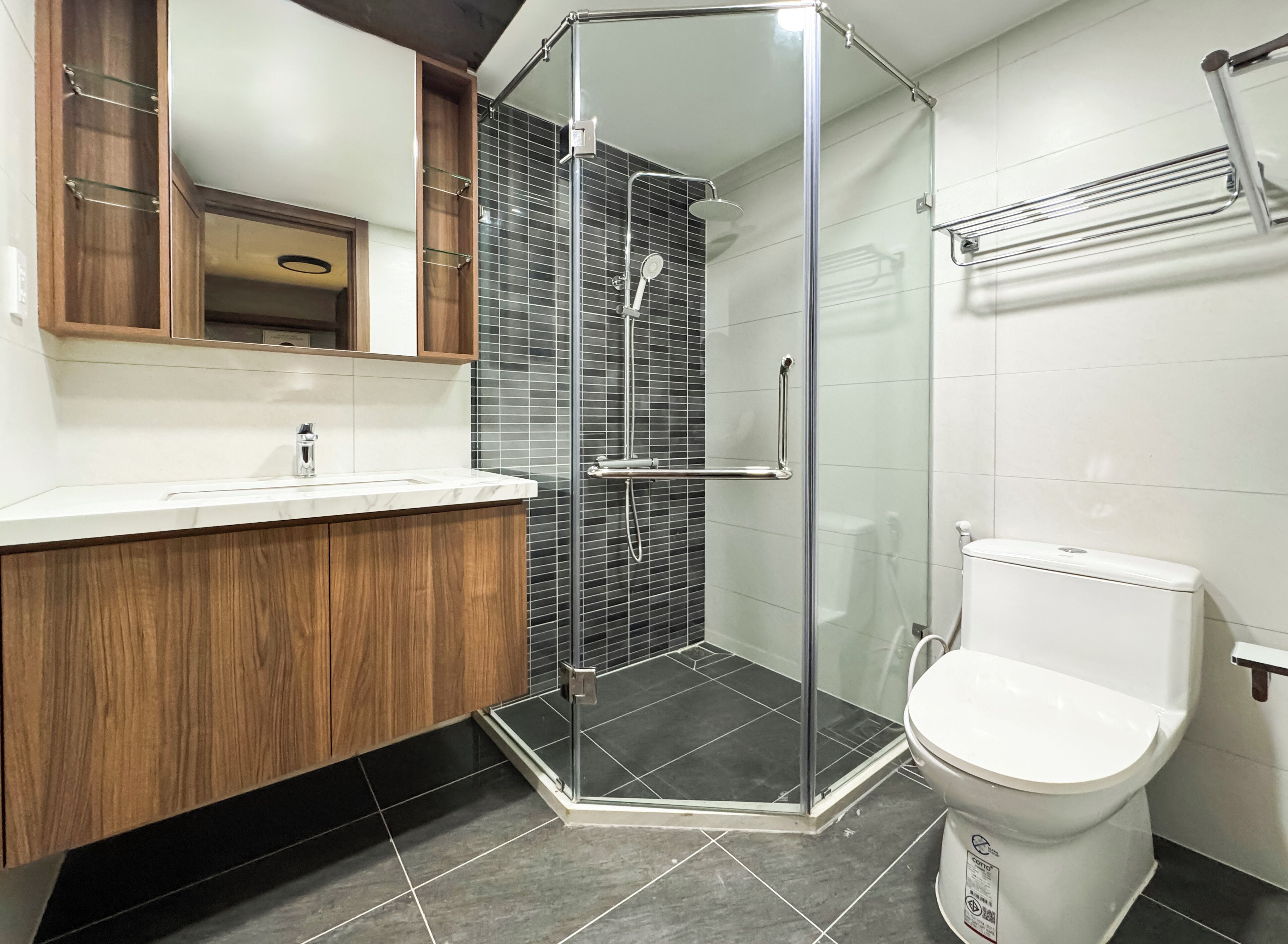 A modern bathroom with a glass-enclosed shower, a wooden vanity, and a white toilet.