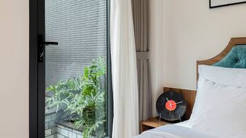Habitación de hotel con cama, tocadiscos y vista a un edificio de ladrillo a través de una puerta de cristal.