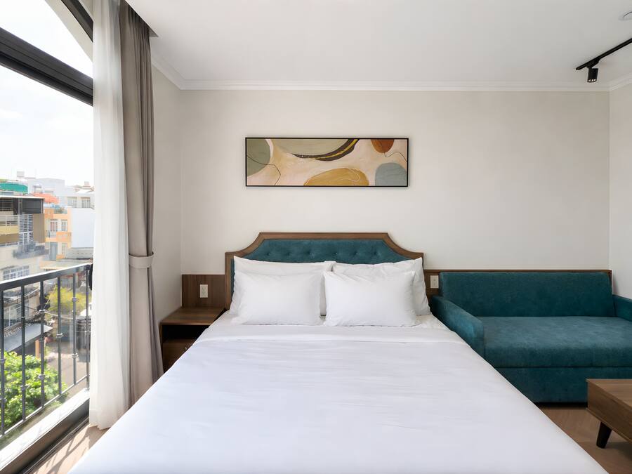 A hotel room with a large bed, a teal sofa, and a city view through a window.