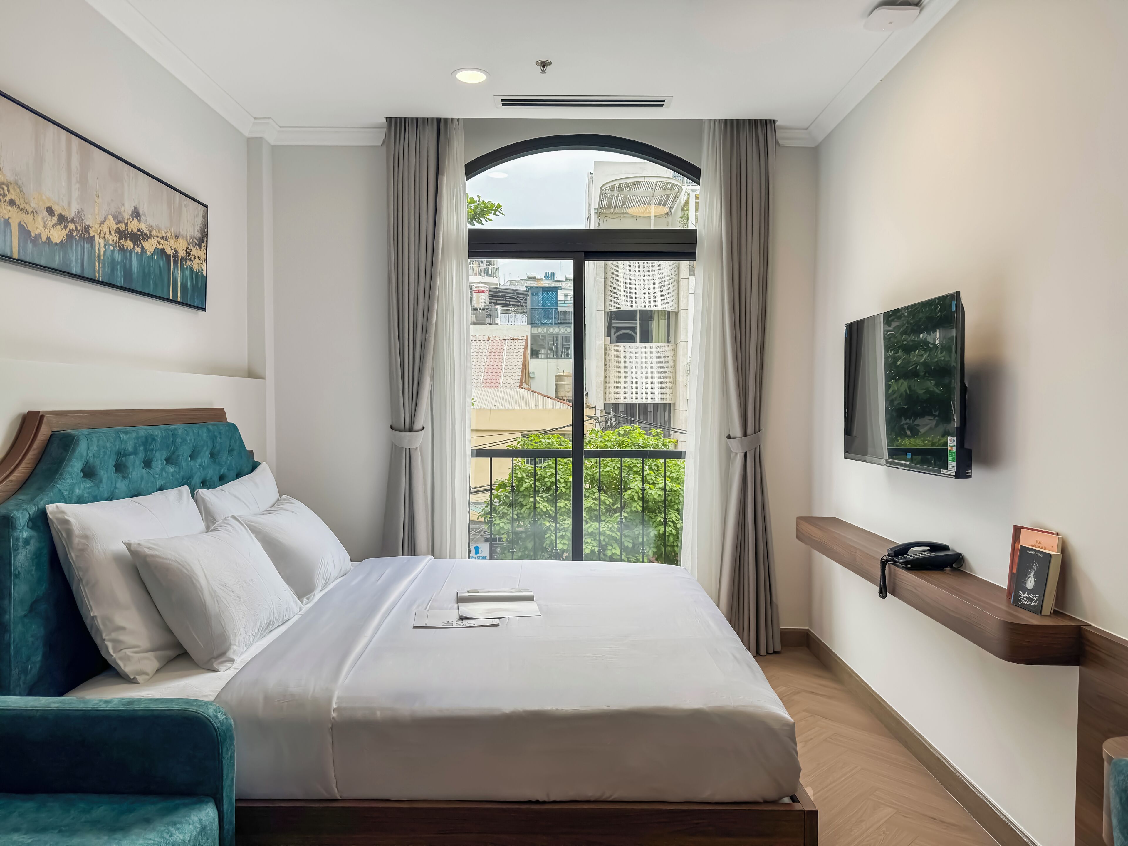 A hotel room with a large bed, a TV mounted on the wall, and a view of the city through the window.