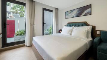 A hotel room with a large bed, a view through a sliding door, a painting on the wall, and a teal armchair.
