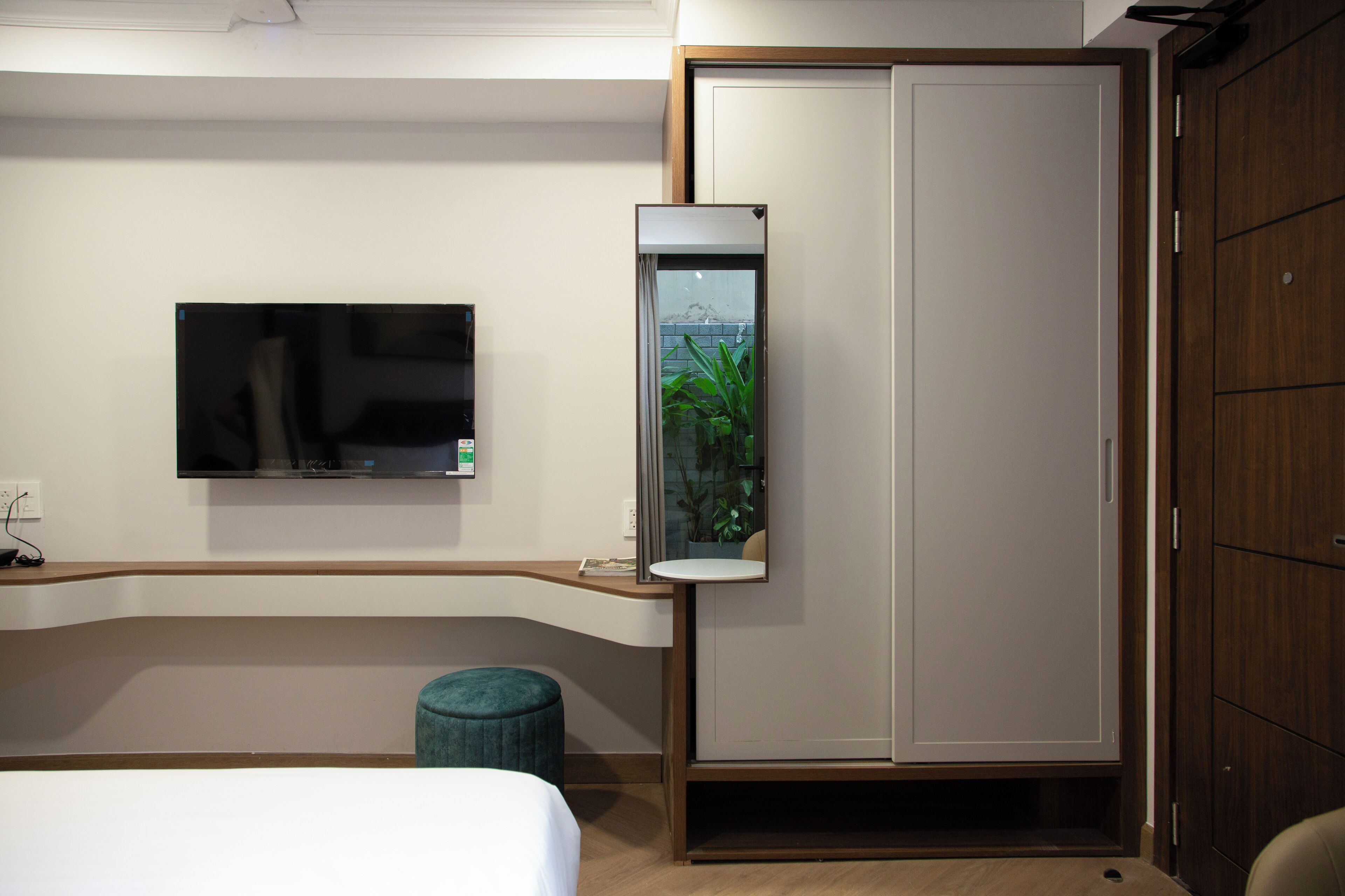 Habitación de hotel con cama, televisión montada en la pared, una pequeña planta en maceta y un armario.