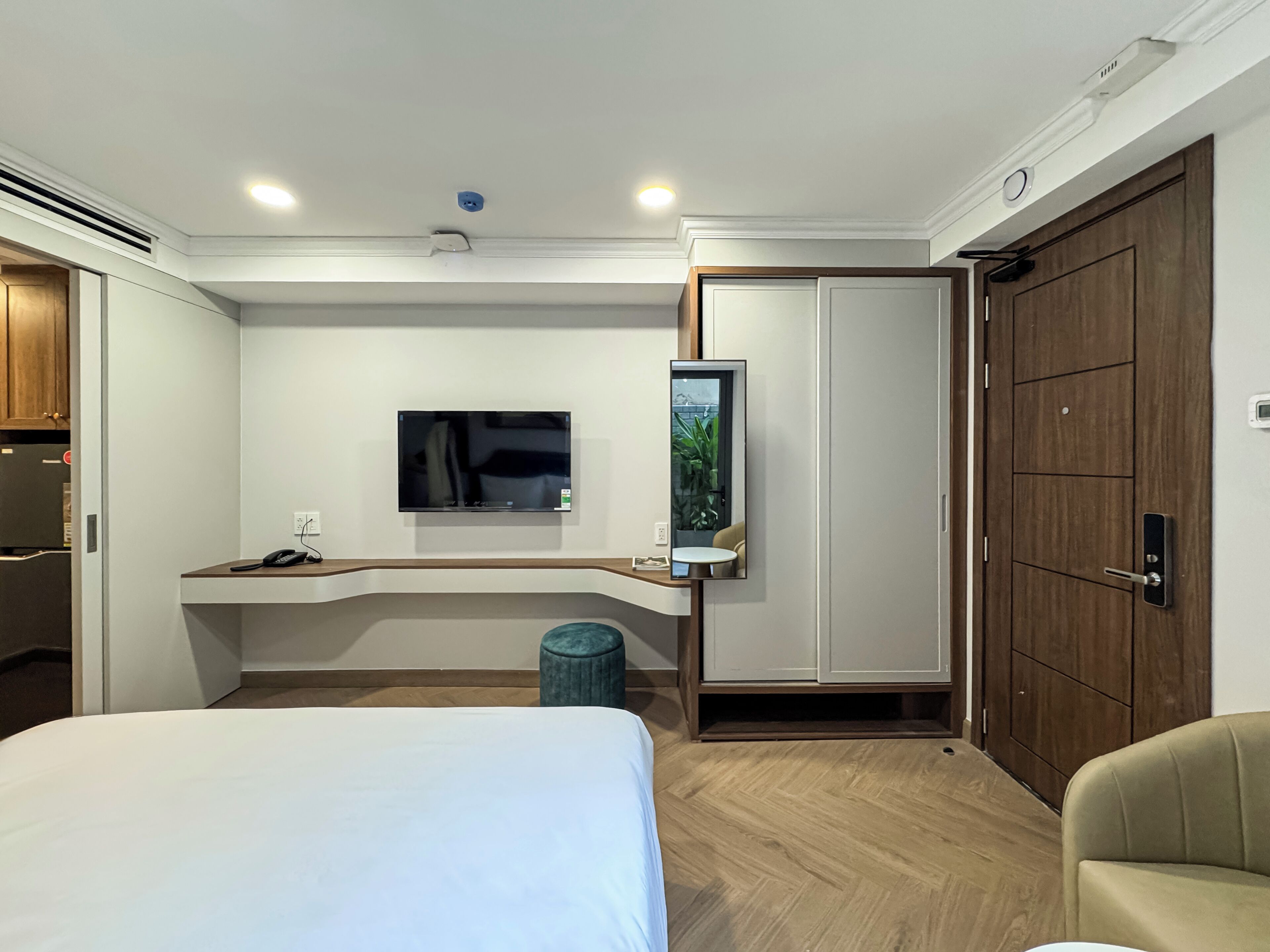 Une chambre d’hôtel comprenant un lit, un bureau avec une télévision, un miroir, une armoire et un petit tabouret.
