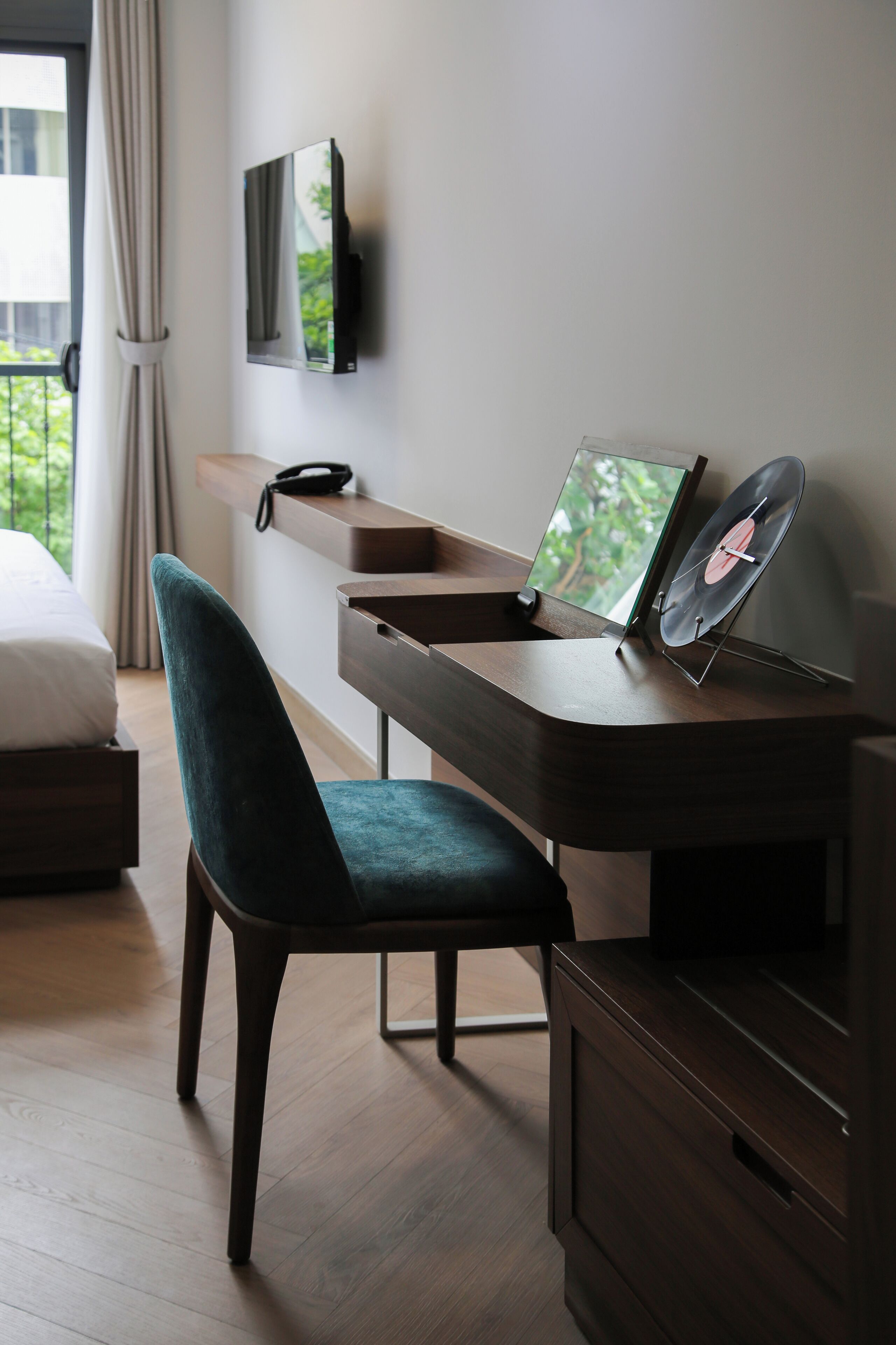 Una habitación de hotel moderna con un escritorio de madera, una silla cómoda, un televisor de pantalla plana montado en la pared y una ventana con cortinas.