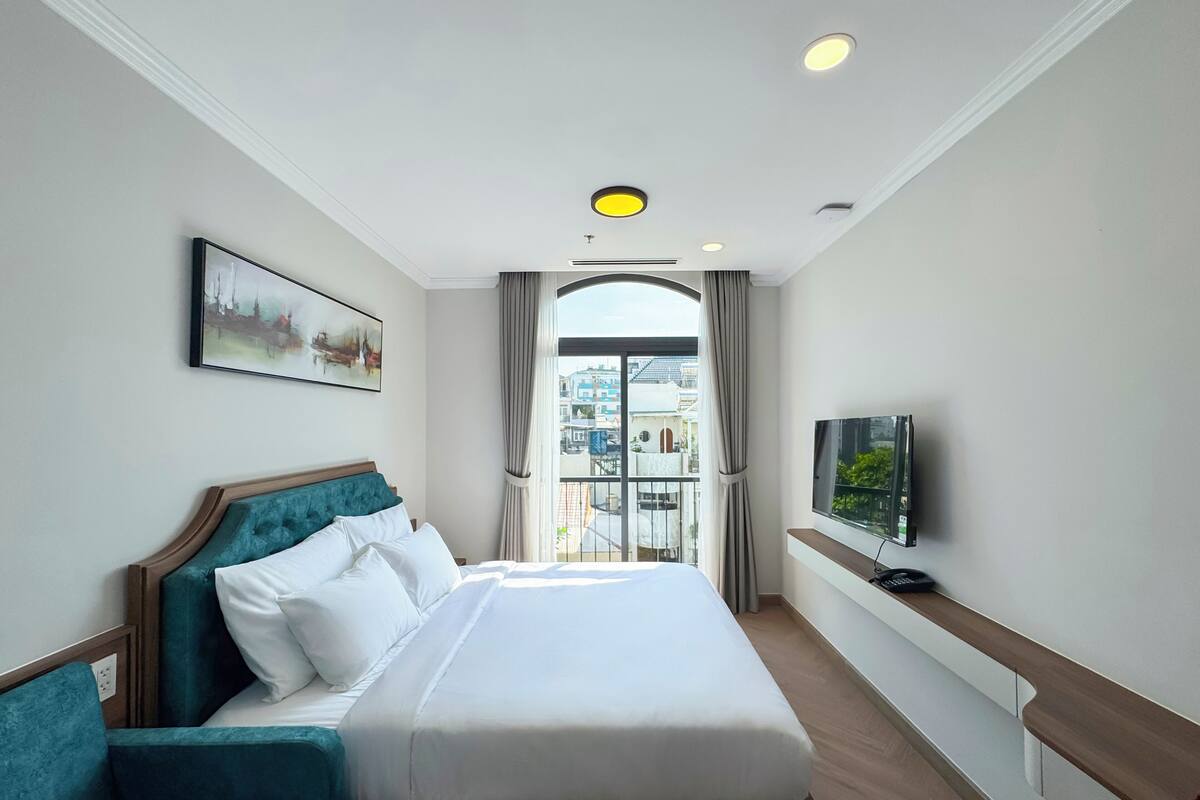 Ein Hotelzimmer mit einem Bett, einem Fernseher, einem Gemälde und Blick auf die Stadt durch das Fenster.