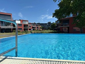 Un espace piscine moderne avec une eau d’un bleu limpide, entouré de bâtiments contemporains dotés de balcons et de grandes fenêtres.