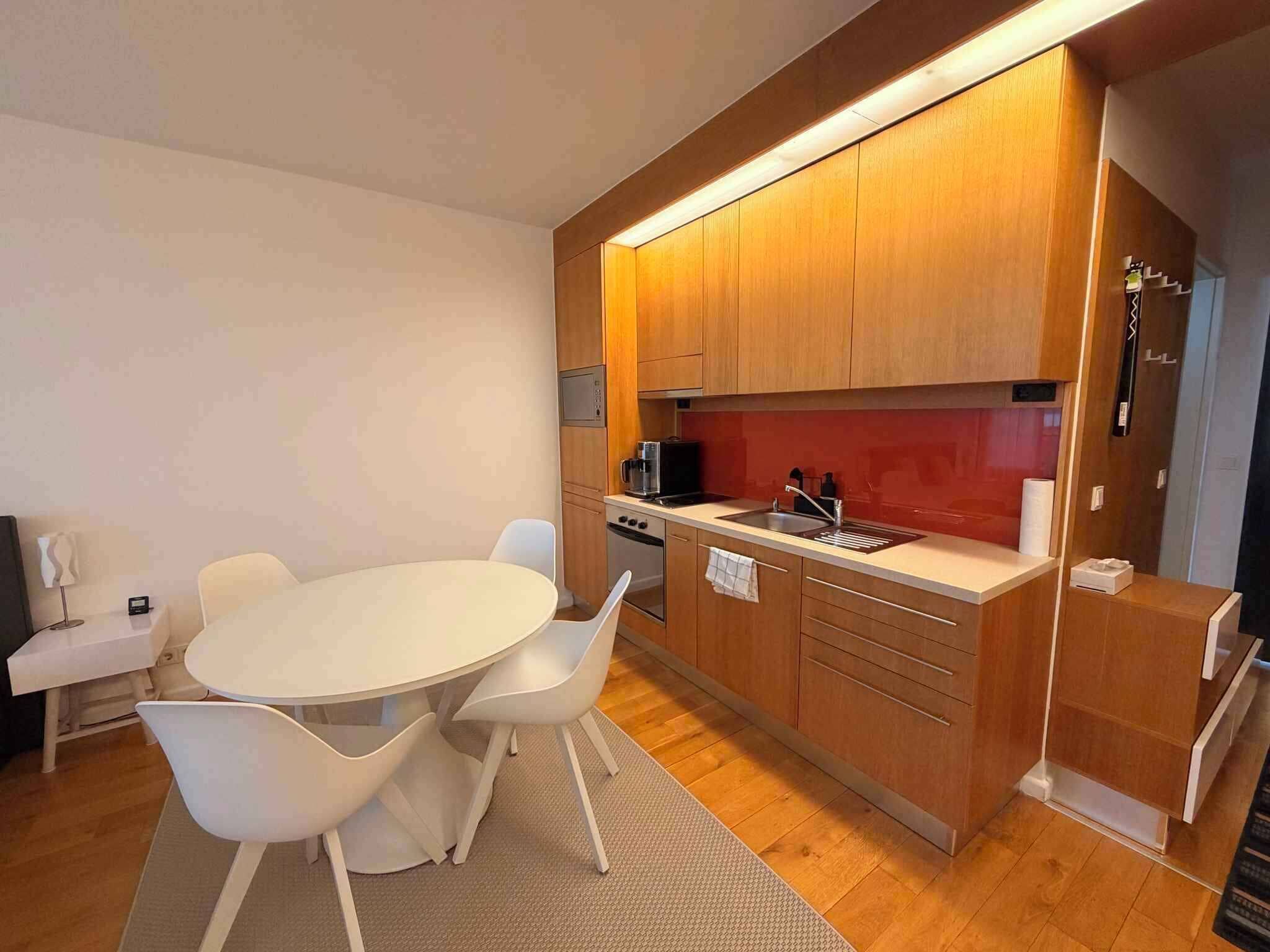 A compact kitchen with wooden cabinets, a white countertop, and a round dining table with chairs.