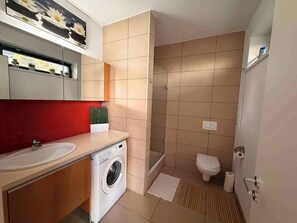 Une salle de bain moderne équipée d’un lave-linge, de toilettes et d’une douche.