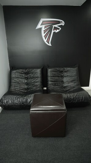 Ein Zimmer mit einer schwarzen Ledersofa, einem passenden Ottomanen und einer Wand mit einem Logo.
