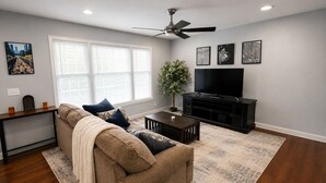 Ein Wohnzimmer mit Sofa, Couchtisch, TV-Schrank und Bildern an den Wänden.