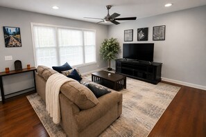 Ein Wohnzimmer mit Sofa, Couchtisch, TV-Schrank und Bildern an den Wänden.