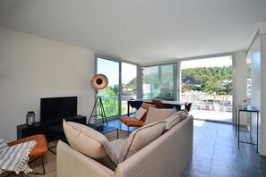 A modern living room with a sofa, a TV, and a large window offering a city view. - Modern apartment near the beach with terrace and sea views (Begur)