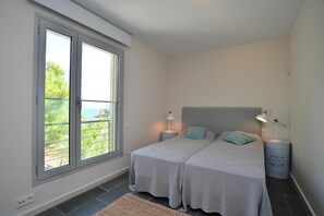 A bedroom with two beds, a large window, a view of greenery, and a bedside lamp. - Modern apartment near the beach with terrace and sea views (Begur)