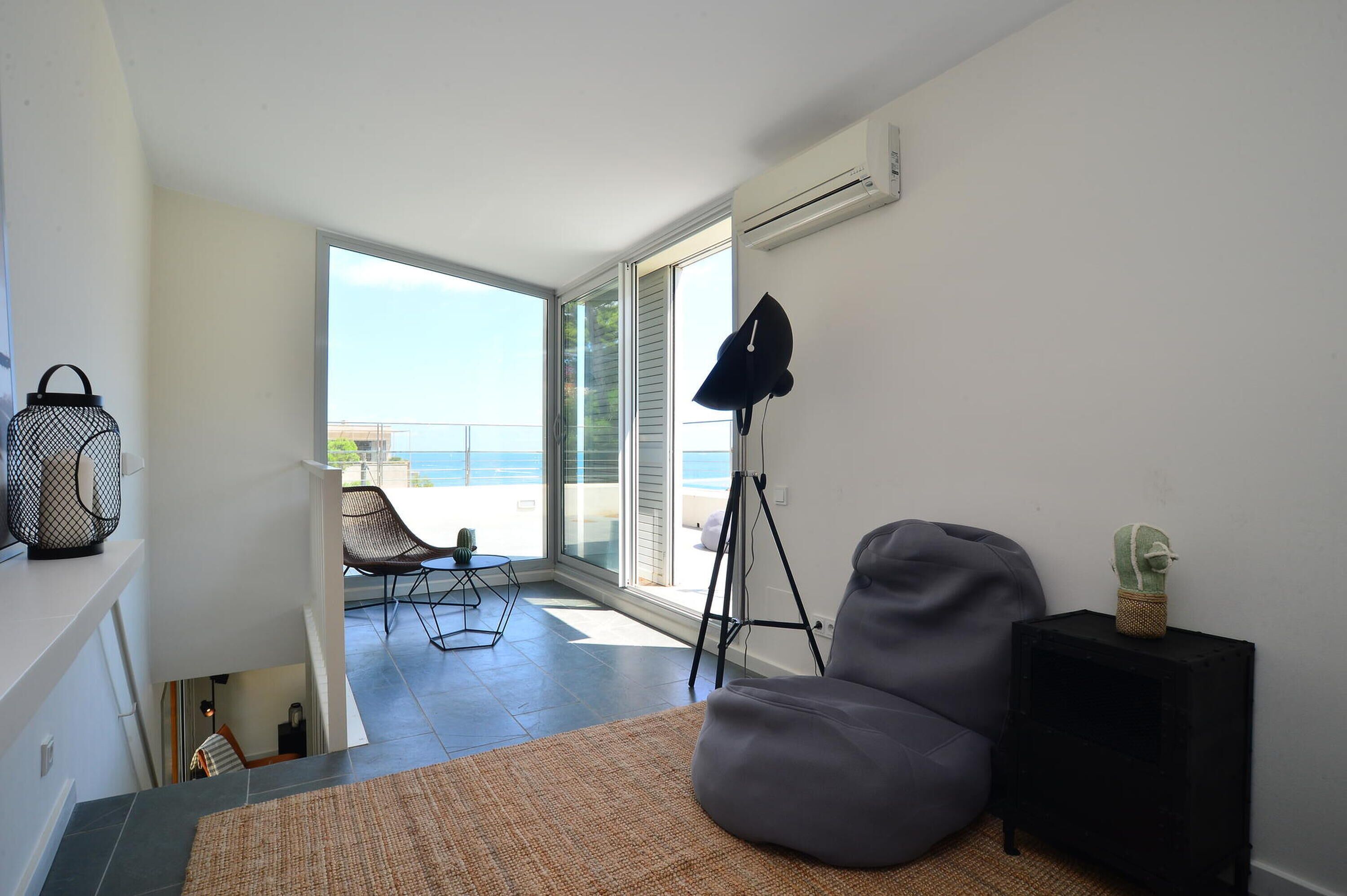 Un salon moderne avec un fauteuil poire gris, une lampe de sol noire et une petite table sur laquelle est posée une plante. On aperçoit, à travers les portes vitrées, un balcon avec une chaise et une table.