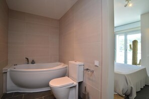A bathroom with a bathtub, toilet, and a bed with a white bedspread. - Modern apartment near the beach with terrace and sea views (Begur)