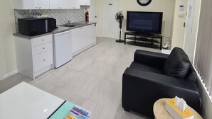 Ein modernes Wohnzimmer mit einem schwarzen Sofa, einem Flachbildfernseher und einem Essbereich mit einem weißen Tisch und Schränken.
