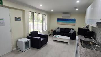 A modern living room with a black sofa, a white coffee table, and a painting of a beach.