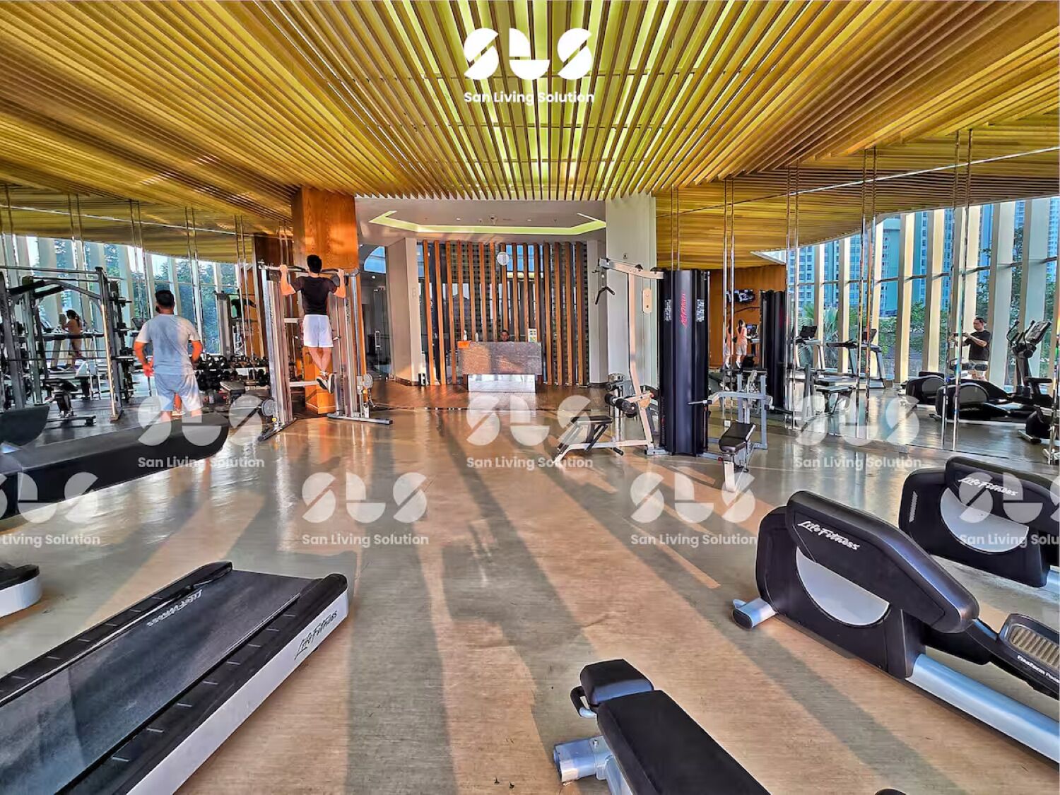 A spacious gym with various exercise equipment, large windows, and a modern wooden ceiling.