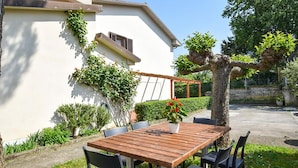 A wooden table and chairs set up outdoors, with a white building in the background and a tree to the right. - Beautiful home in Lari with outdoor swimming pool (Lari)