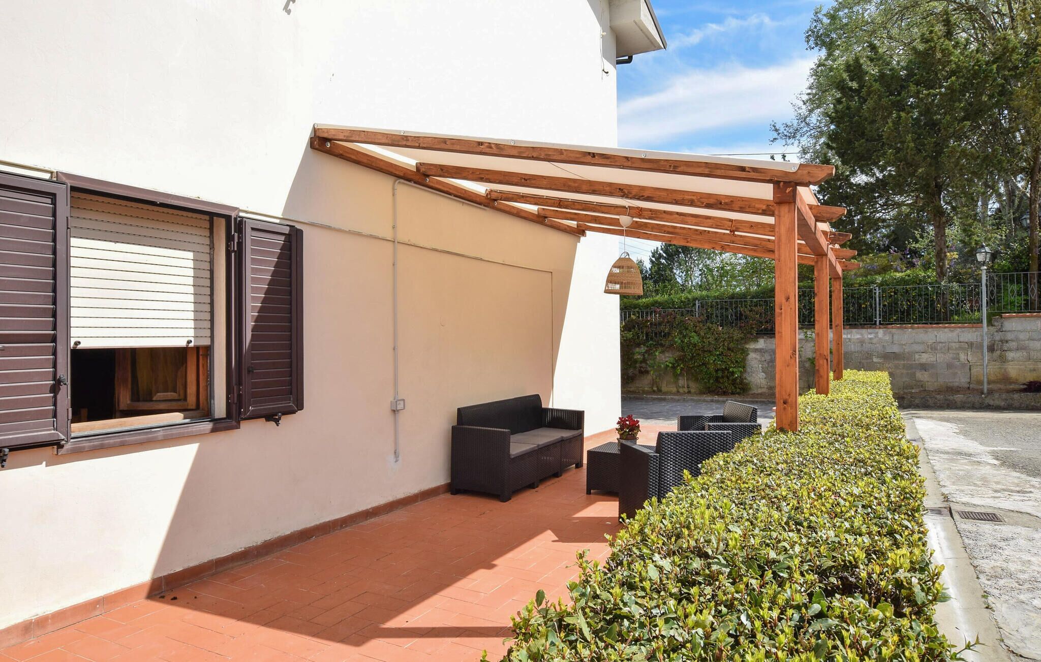 A covered patio area with a pergola, outdoor seating, and a hedge.