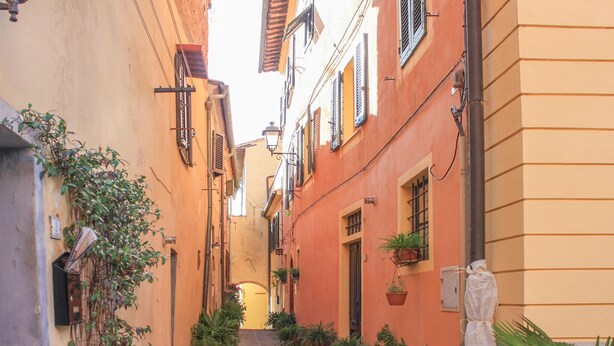 A narrow alleyway with buildings on either side, featuring balconies with potted plants and a statue in the foreground. - Beautiful home in Lari with outdoor swimming pool (Lari)