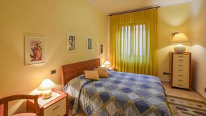 A bedroom with a bed, two bedside lamps, a nightstand, a chair, a dresser, and a window with yellow curtains. - Cozy apartment in Calci (Calci)