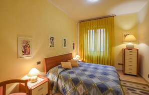 A bedroom with a bed, two bedside lamps, a nightstand, a chair, a dresser, and a window with yellow curtains. - Cozy apartment in Calci (Calci)