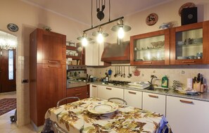 A kitchen with wooden cabinets, a stove, and a dining table set with plates. - Cozy apartment in Calci (Calci)