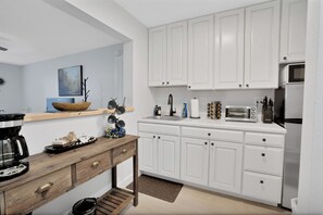 A modern kitchen with white cabinets, a wooden table, and various appliances including a coffee maker and toaster.