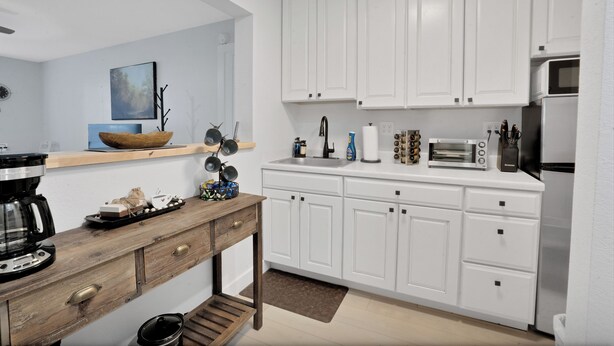 Een moderne keuken met witte kastjes, een houten tafel en diverse apparaten, waaronder een koffiezetapparaat en een broodrooster.