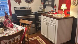 A compact kitchen with a stove, sink, and white cabinets. There is a red door and a small table with chairs. - Charming 2-Bedroom House in the Heart of Round Top (Round Top)