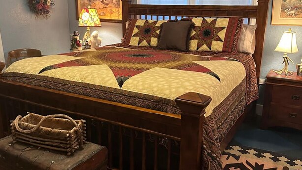 A bedroom with a large bed, a wooden headboard, a nightstand with a lamp, a decorative rug, and a small chest of drawers. - Charming 2-Bedroom House in the Heart of Round Top (Round Top)