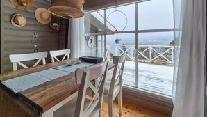 A wooden dining table with white chairs, a woven basket hanging above, and a view of a snowy landscape through large windows. - 3 bedroom beautiful home in Fjelberg (Fjelberg)