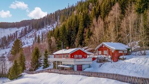 Una baita di legno rossa con un balcone, circondata da una staccionata di legno e terreno innevato.