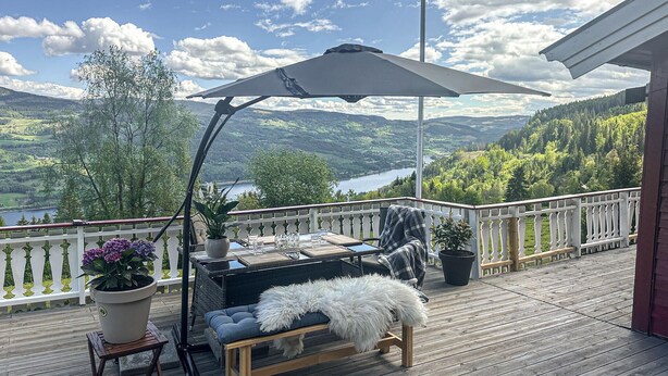 Un terrazzo in legno con tavolo e sedie, una pianta in vaso e vista su un lago e montagne.