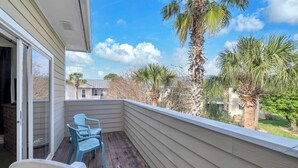 A balcony with a view of palm trees and houses, a sliding glass door, and two chairs. - Private Beach Access-Pool-Central Destin BP1003 (Destin)