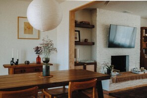 Un coin repas avec une table en bois, des chaises, un vase de fleurs et un téléviseur fixé au mur.