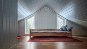 Un dormitorio tipo loft con techo inclinado, una cama de madera y dos ventanas.