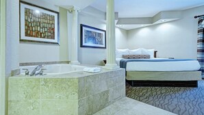 Une chambre d’hôtel avec une grande baignoire, un lit agrémenté d’un coussin à motifs et deux œuvres d’art encadrées au mur.