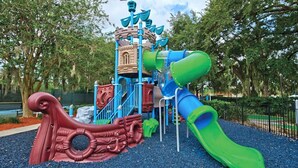 Une aire de jeux avec un toboggan, des structures d’escalade et un élément décoratif en forme de bateau.