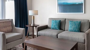 Een moderne hotelkamer met een grijze zithoek, een houten salontafel en een lamp.
